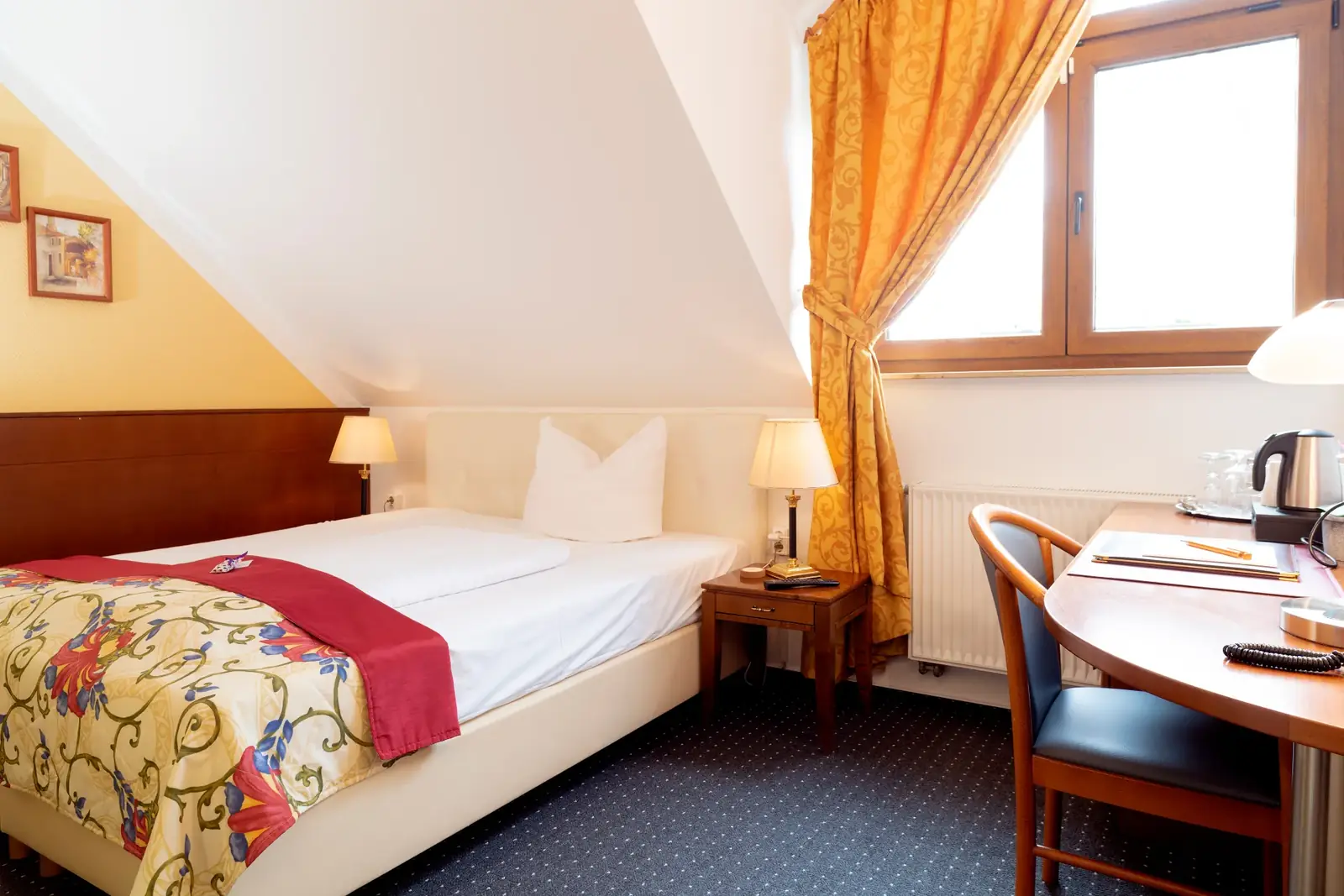 Standard room under the sloping roof with bed, window and small table – Hotel am Katharinenholz