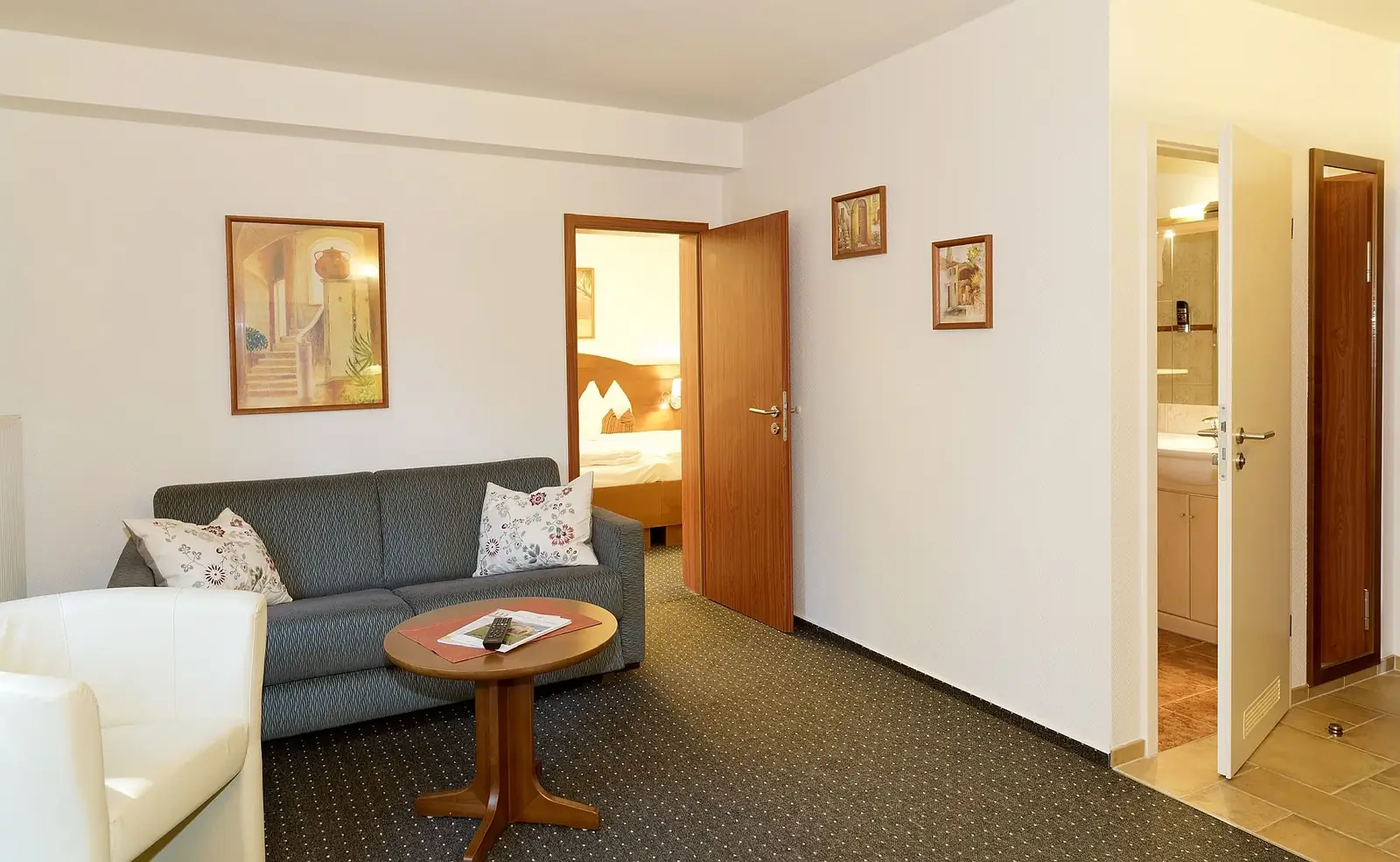 Wohnbereich der Suite mit Sofa, Sessel und Blick in Schlafzimmer und Bad – Hotel Potsdam am Katharinenholz