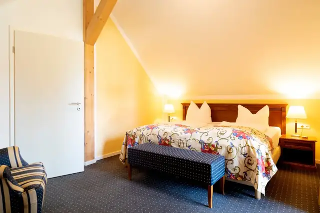 Sleeping area of the attic suite with double bed, bed bench and armchair – Hotel am Katharinenholz Potsdam