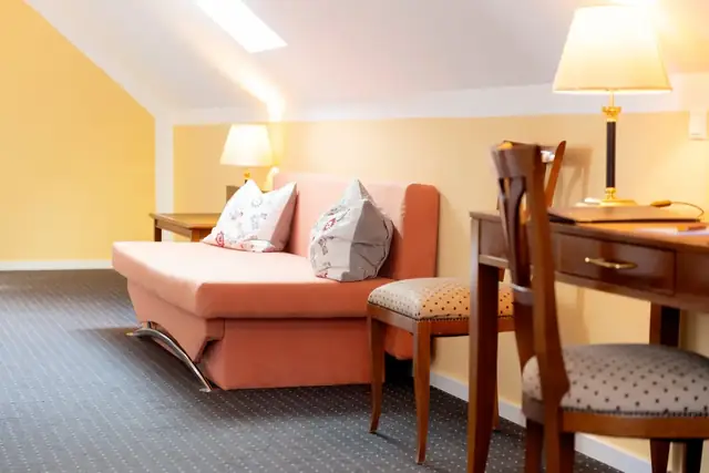 Sofa and desk under the sloping ceiling in the suite – Hotel am Katharinenholz Potsdam