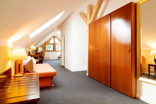 Open-plan living area of the attic suite with sofa, wardrobe and skylights – Hotel am Katharinenholz Potsdam