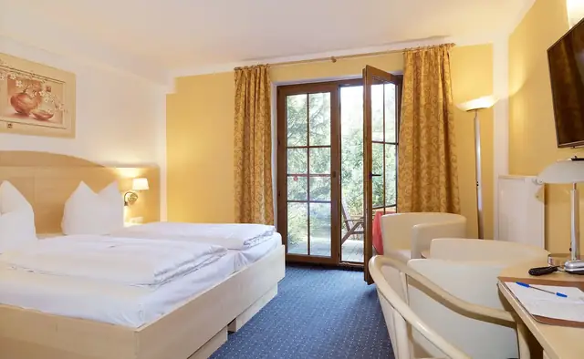 Doppelzimmer mit Bett, Sitzgruppe und Terrassentür zum Hotelgarten – Hotel Potsdam am Katharinenholz