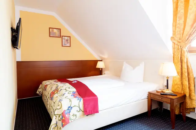 Standard room with bed, flat-screen TV on the wall and bedside lamps – Hotel am Katharinenholz