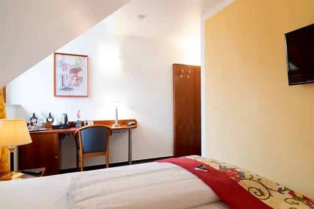 Desk with chair, coffee station, wardrobe and flat-screen TV in the standard room – Hotel am Katharinenholz