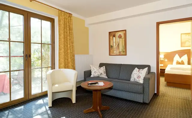 Wohnzimmer der Suite mit Schlafsofa, Sessel und Terrassentür – Hotel Potsdam am Katharinenholz