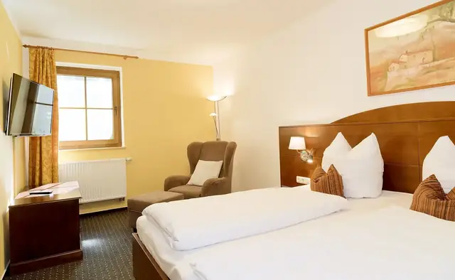 Schlafbereich der Suite mit Doppelbett, Ohrensessel und Flat-TV – Hotel Potsdam am Katharinenholz